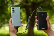 Close-up of hands holding a smartphone connected to a power bank outdoors.