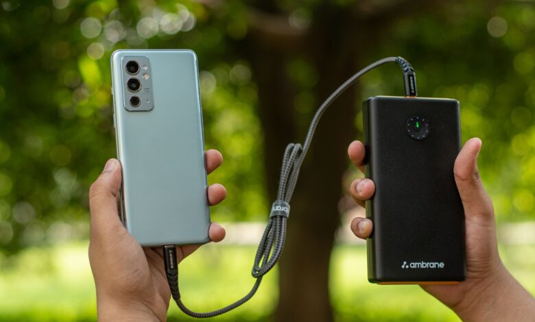 Close-up of hands holding a smartphone connected to a power bank outdoors.