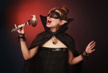 Mysterious woman dressed as a vampire with a gothic mask and cape, holding a fork