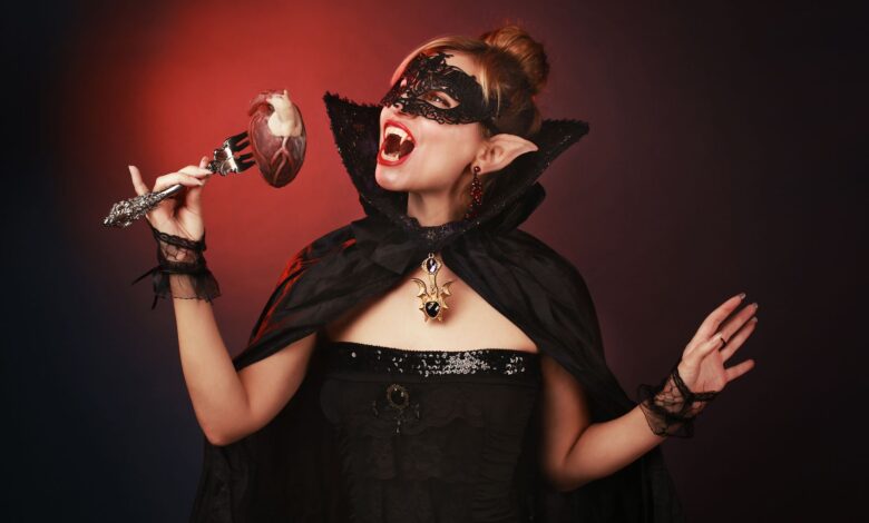 Mysterious woman dressed as a vampire with a gothic mask and cape, holding a fork