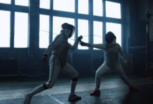 Two fencers engaged in a close indoor duel, showcasing dynamic action and skill.