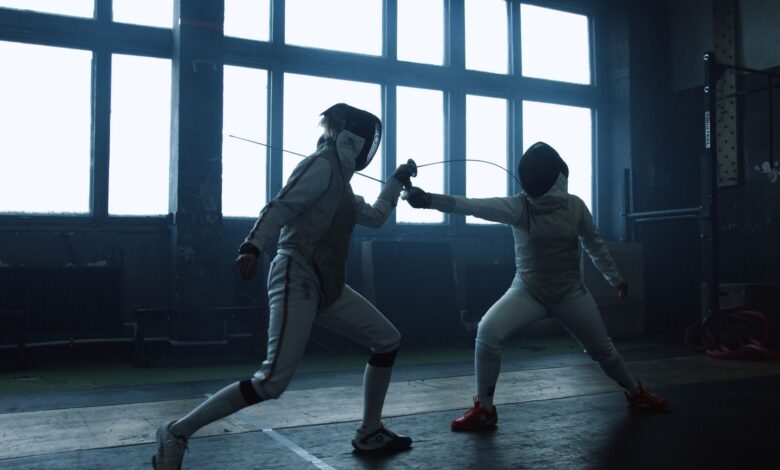 Two fencers engaged in a close indoor duel, showcasing dynamic action and skill.