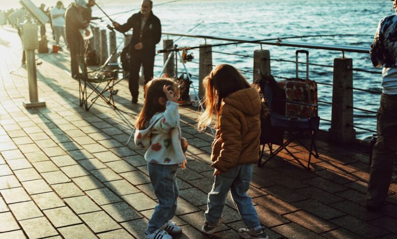 Two children play by the Bosphorus in Istanbul at sunset, with fishermen nearby.