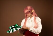 A cosplay portrait of an elf with pink hair and green accessories in a studio setting.