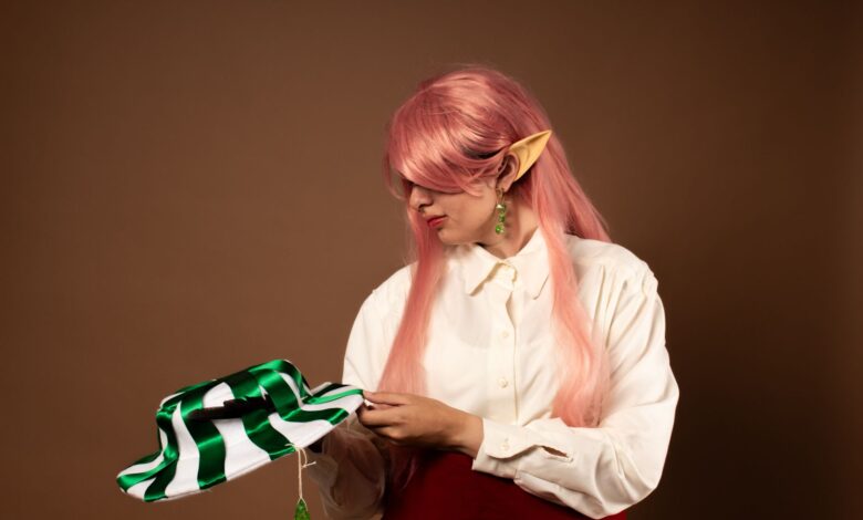 A cosplay portrait of an elf with pink hair and green accessories in a studio setting.