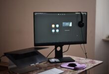 Contemporary computer with headphones hanging on monitor placed on table with laptop keyboard and mouse at convenient workplace in room