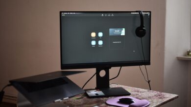 Contemporary computer with headphones hanging on monitor placed on table with laptop keyboard and mouse at convenient workplace in room