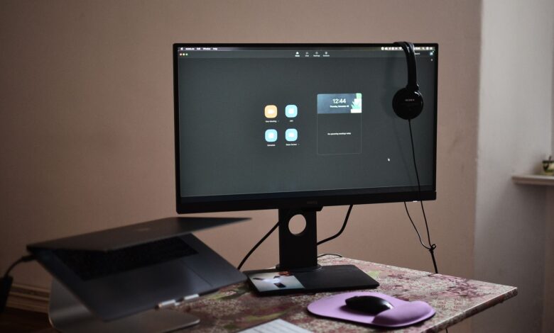 Contemporary computer with headphones hanging on monitor placed on table with laptop keyboard and mouse at convenient workplace in room