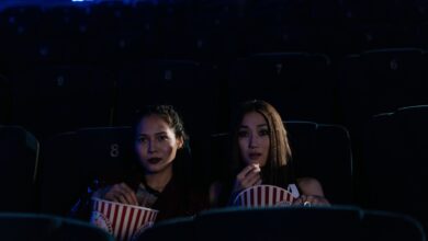 Two women sitting in a dark cinema, enjoying popcorn and watching a movie.