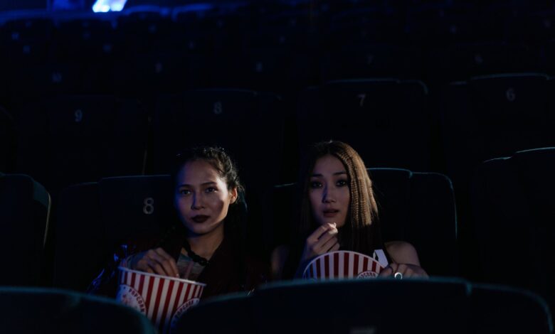 Two women sitting in a dark cinema, enjoying popcorn and watching a movie.