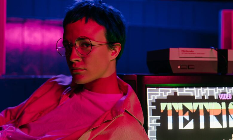 A teenager with eyeglasses in an 80s-style arcade displaying a Tetris game on screen.