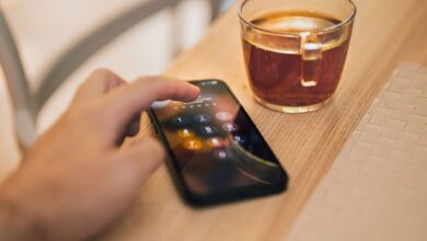 Close-up of hand unlocking a smartphone next to a cup of tea on a wooden table, emphasizing technology and security.
