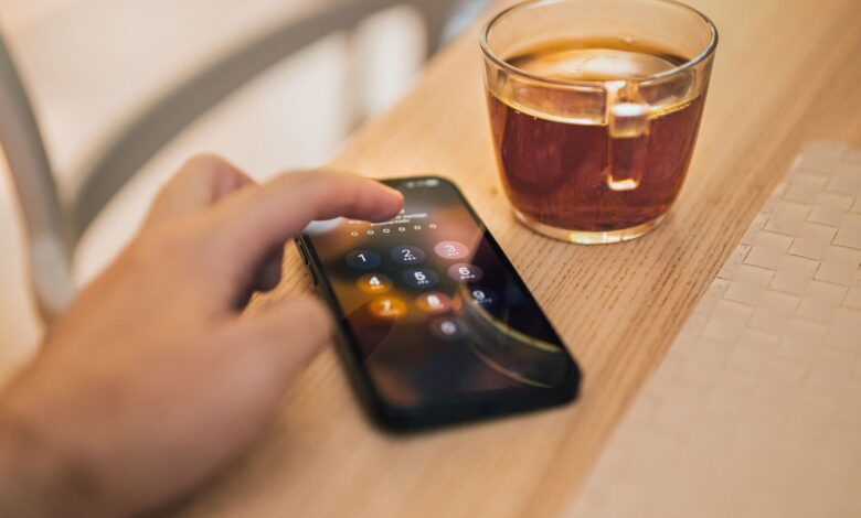 Close-up of hand unlocking a smartphone next to a cup of tea on a wooden table, emphasizing technology and security.