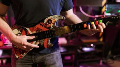 Close-up of a man playing a Guitar Hero controller indoors, featuring vibrant colors and technology.
