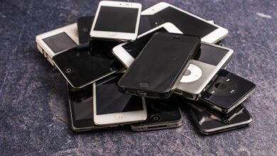 Stack of assorted aged cellphones with black screens and portable music players on gray background
