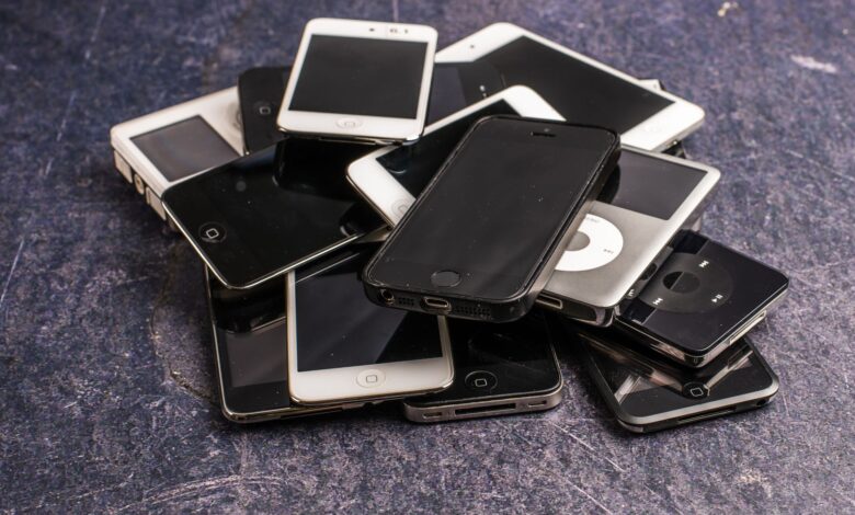 Stack of assorted aged cellphones with black screens and portable music players on gray background