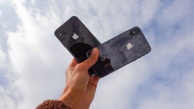 Close-up of a hand holding two smartphones against a cloudy sky, showcasing modern technology.