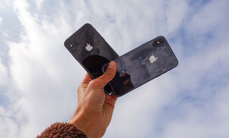 Close-up of a hand holding two smartphones against a cloudy sky, showcasing modern technology.