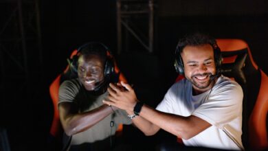 Two young male gamers celebrating a victory with a handshake and smiles in a dark gaming room.