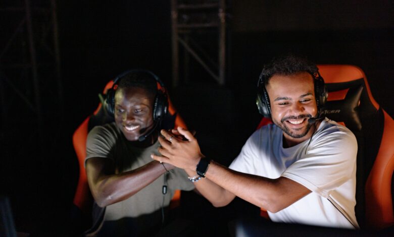 Two young male gamers celebrating a victory with a handshake and smiles in a dark gaming room.