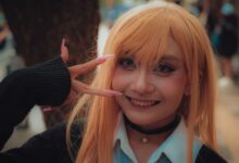 A vibrant cosplay portrait of a young adult in costume posing with a peace sign outdoors.