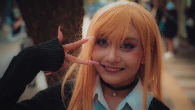 A vibrant cosplay portrait of a young adult in costume posing with a peace sign outdoors.