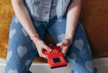 A person holding vintage video game console wearing heart-pattern denim and bracelets.