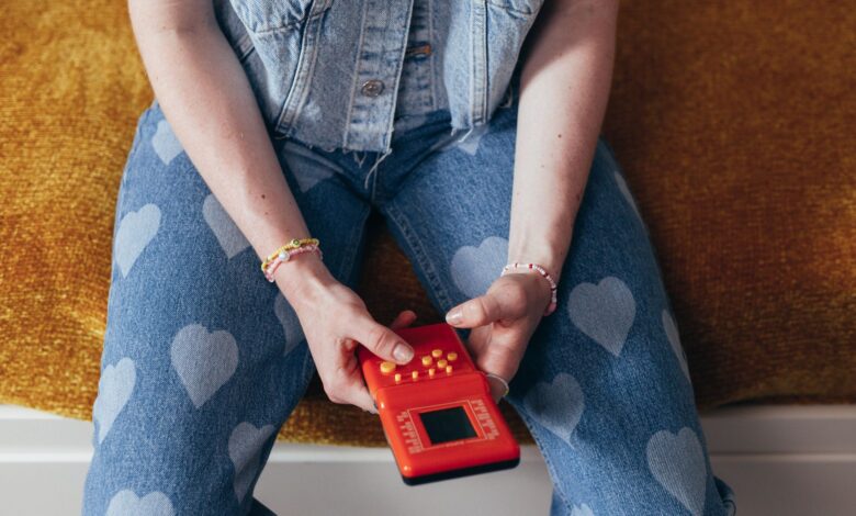 A person holding vintage video game console wearing heart-pattern denim and bracelets.