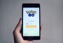 Smartphone displaying Pokémon Go app sign-in screen, held in hand.