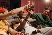 A group of friends sitting on a couch, toasting with beers during a casual game night.