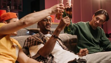 A group of friends sitting on a couch, toasting with beers during a casual game night.