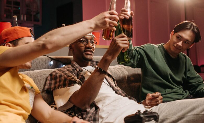 A group of friends sitting on a couch, toasting with beers during a casual game night.