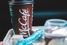 Delicious coffee in dark red cup with lid placed in cup holder with blue shiny wrapper and plastic cup