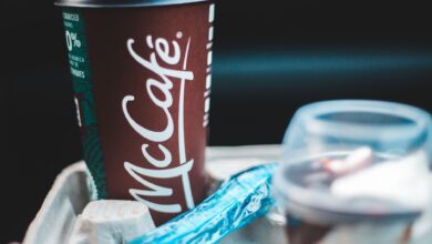 Delicious coffee in dark red cup with lid placed in cup holder with blue shiny wrapper and plastic cup