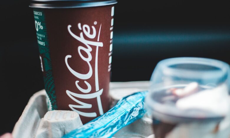 Delicious coffee in dark red cup with lid placed in cup holder with blue shiny wrapper and plastic cup