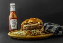 Mouth-watering gourmet burger with cheese and ketchup on wooden plate.