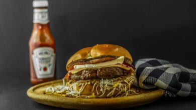 Mouth-watering gourmet burger with cheese and ketchup on wooden plate.