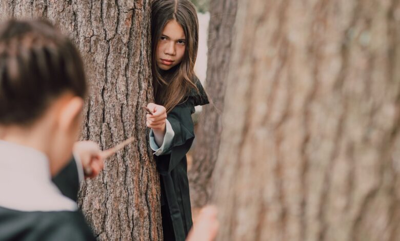 Children dressed as wizards play with magic wands in a forest setting, evoking fantasy and adventure.