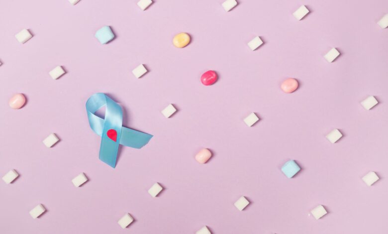 A blue diabetes awareness ribbon surrounded by candies on a pink pastel background promoting health awareness.