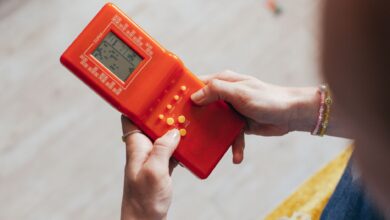 Hands holding a retro red handheld game console, playing a classic game.