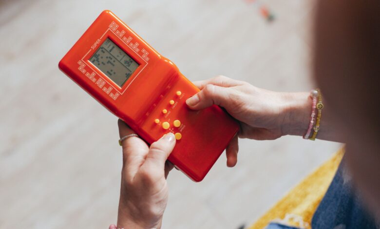Hands holding a retro red handheld game console, playing a classic game.