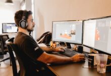A man wearing headphones works on a computer with two monitors in a modern office setup.