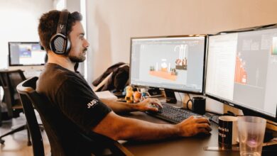 A man wearing headphones works on a computer with two monitors in a modern office setup.