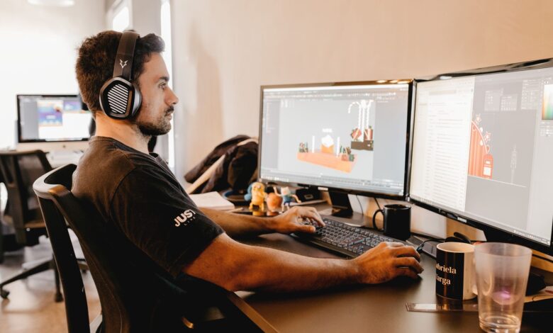 A man wearing headphones works on a computer with two monitors in a modern office setup.