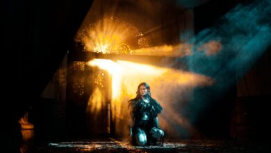 A young woman kneels in dramatic light and shadows, creating an ethereal atmosphere.