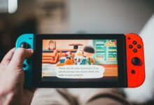 Crop anonymous person playing videogame while using game console and sitting at home on blurred background
