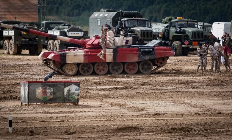 A military training exercise featuring tanks and soldiers on a field, showcasing armored vehicle operations.