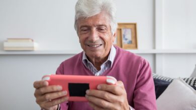 Elderly man smiling while playing on a handheld console indoors.