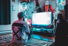 Back view of anonymous male sitting on floor near modern monitor and playing video game in room with comic stuff