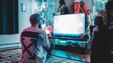 Back view of anonymous male sitting on floor near modern monitor and playing video game in room with comic stuff